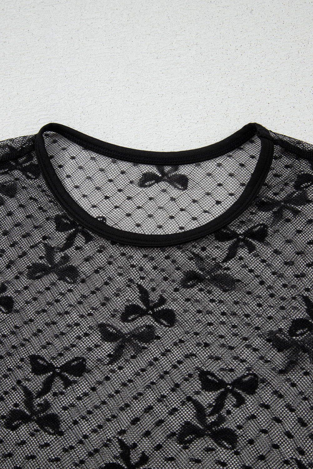 Close-up of the neckline of a sheer black lace blouse featuring a bow pattern and a contrasting black trim