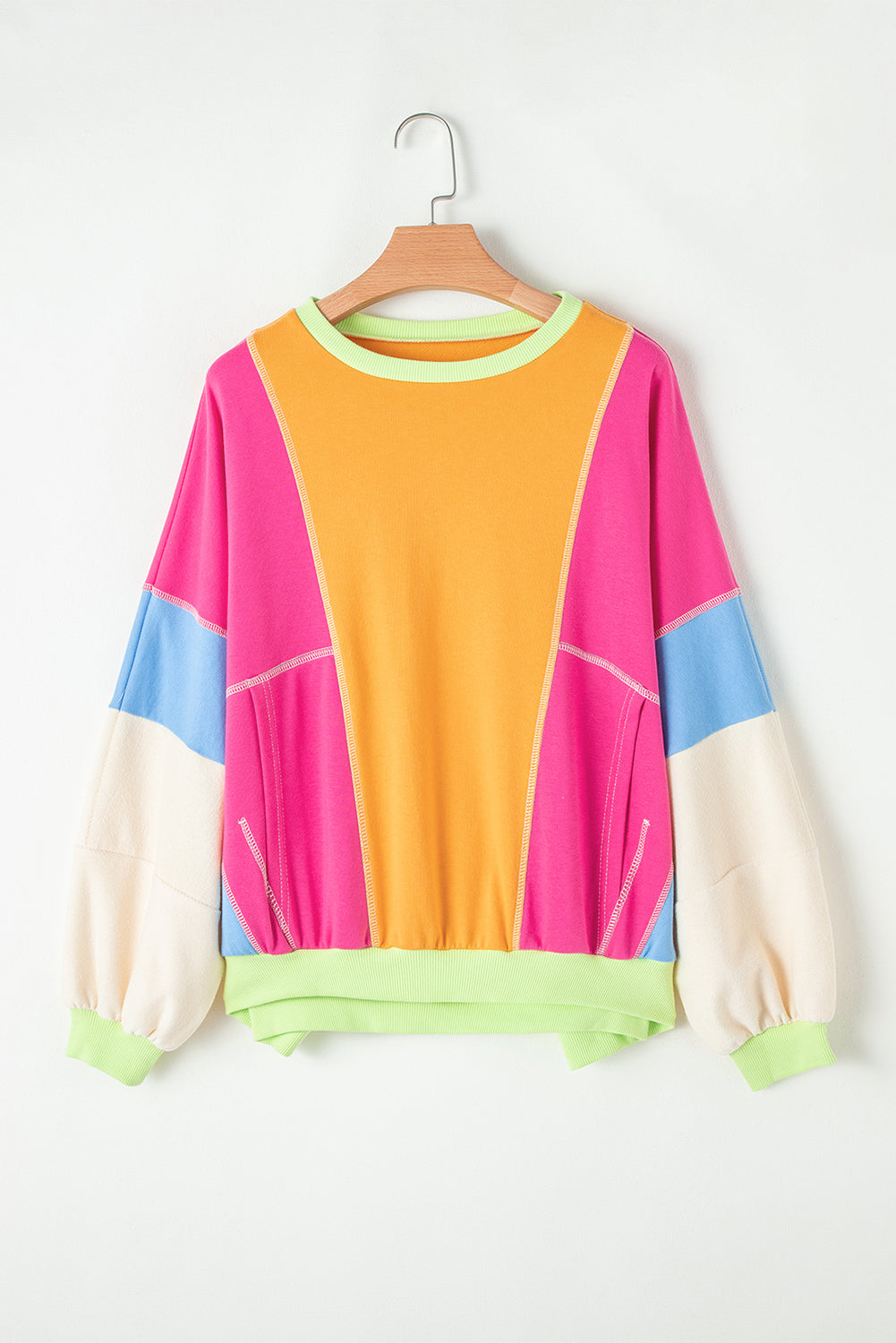 Front view of a vibrant colorblock sweatshirt featuring bold colors: pink, orange, and blue, hanging on a wooden hanger.
