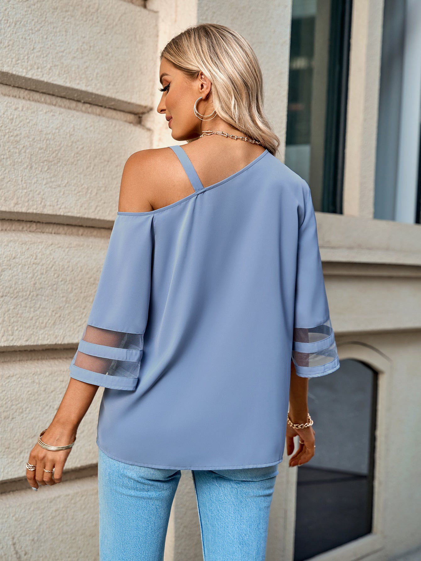 Back view of a model Wearing a Dusty Blue Ladies Asymmetrical Neck Sheer Striped Flare Sleeve Blouse